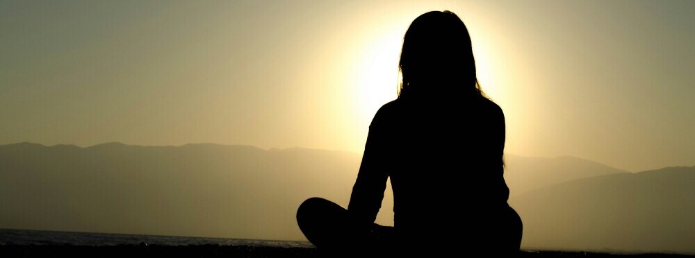 A woman sitting crossed leg looking at the sunrise or sunset